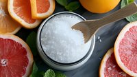 Fresh citrus bath salt with grapefruit, orange slices and mint leaves on dark background. Natural spa and aromatherapy concept for wellness and skincare.