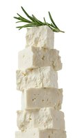 Stacked fresh white cheese cubes with rosemary herb garnish on top, isolated on white background. Suitable for food photography, culinary blogs, recipe websites, and cooking publications.