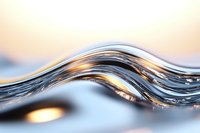 Flowing liquid wave with golden sunlight reflections creates dynamic curves and ripples against blurred background, capturing motion and light interplay.