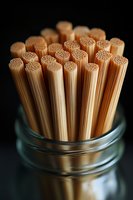 Raw spaghetti pasta strands standing upright in glass jar against dark background, showing detailed ends and golden color in dramatic lighting.