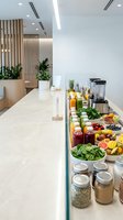 Modern juice bar counter with fresh fruits, vegetables, smoothie ingredients and blender in contemporary wellness cafe interior with wooden accents and plants.