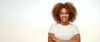 Young African American woman with curly hair smiling confidently with arms crossed wearing white t-shirt against neutral background for business portrait.