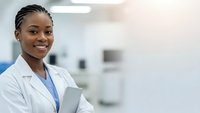 Smiling African American female doctor in white coat holding tablet in modern medical office with copy space for healthcare and medicine concepts.
