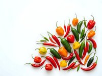 Colorful hot chili peppers scattered on white background. Fresh spicy vegetables in red, orange, yellow and green colors isolated for cooking design.