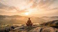 Young Asian man meditating in lotus position on mountain peak at sunrise with terraced fields and misty valleys below creating peaceful spiritual atmosphere.