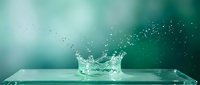 Water splash crown with droplets on glass surface against turquoise gradient background for refreshing beverage and purity concepts.