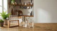 Laboratory glassware and test tubes on wooden table in bright modern kitchen setting for scientific research and experimentation at home.