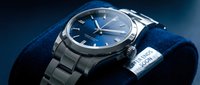 Elegant silver stainless steel wristwatch with deep blue dial resting on navy velvet surface, showcasing luxury timepiece craftsmanship and modern design.