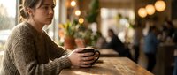 Young woman in cozy sweater holding coffee cup in warm cafe with bokeh lights, perfect for lifestyle and hospitality marketing materials.