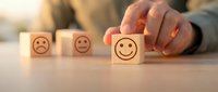 Hand selecting wooden block with happy face emoticon from sad to positive feedback rating scale for customer satisfaction survey and service quality.