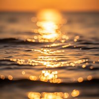 Golden sunset over ocean waves with sparkling bokeh light reflections on water surface creating dreamy atmospheric seascape for relaxation and meditation.