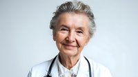 Senior female doctor with gray hair and stethoscope smiling confidently in white medical coat against neutral background for healthcare concepts.