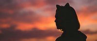 Silhouette of young woman with hair bun against dramatic orange sunset sky with clouds. Peaceful moment capturing serenity and contemplation at golden hour.
