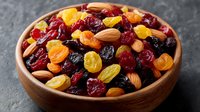 Colorful mix of dried fruits and nuts in wooden bowl including cranberries, raisins, almonds and apricots for healthy snacking and cooking recipes.