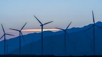 Wind turbines generating renewable energy at sunset with mountain silhouettes creating sustainable power landscape for clean electricity production.