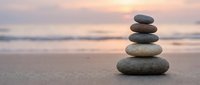 Balanced stone stack on sandy beach at sunset creating peaceful zen meditation scene with soft ocean waves and golden sky for wellness and mindfulness concepts.