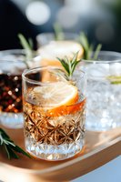 Craft cocktail with lemon slice and fresh rosemary in crystal glass on wooden tray. Elegant drink with bokeh background, close-up view for bar menu and mixology.