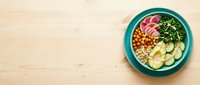 Colorful Buddha bowl with fresh vegetables, chickpeas, and greens in turquoise ceramic dish on wooden surface for healthy eating and nutrition.