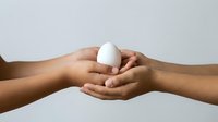 Two hands holding white egg together on neutral background, isolated for design use on packaging, advertising, nutrition education, cooking blogs, and wellness content.