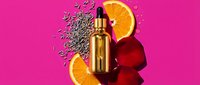 Vitamin C serum bottle with orange slices and seeds on vibrant pink background for skincare and beauty product advertising campaigns.