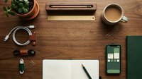 Organized wooden desk workspace with laptop, smartphone, coffee cup, plant and office supplies arranged for productivity and business planning.
