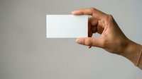 Male hand of South Asian ethnicity holding blank white business card or paper against neutral gray background, suitable for branding, corporate identity, and marketing materials.