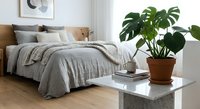 Modern minimalist bedroom interior with gray bedding, wooden headboard, and green monstera plant in terracotta pot on white marble table for home decor inspiration.