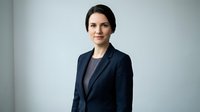 Professional businesswoman in navy suit smiling confidently in modern office setting for corporate presentations and business communications.