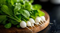 Fresh white baby turnips with bright green leaves arranged in row on rustic wooden cutting board against dark background, macro food photography.
