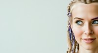 Young woman with fair skin and light eyes wearing decorative braids with beads, smiling at camera against neutral background. Suitable for beauty, hairstyle, and lifestyle marketing.