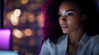 Young African American woman with natural curly hair and professional attire gazing confidently against blurred purple and gold bokeh background lighting.