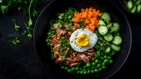 Healthy quinoa bowl with soft-boiled egg, fresh vegetables, carrots, cucumber, peas and herbs on dark background for nutritious meal planning.