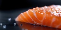 Fresh raw salmon fillet with water drops on black surface, macro close up view showing texture and natural orange color of premium seafood.