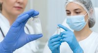 Female medical professionals in protective gear examining vaccine vial in clinical laboratory setting for healthcare research and pharmaceutical development.