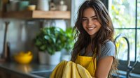 Young Hispanic woman in yellow apron holding fresh bananas in modern kitchen with natural lighting, expressing joy and positivity while preparing healthy breakfast.
