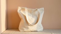 Blank natural canvas tote bag with handles on neutral beige background, ready for custom printing, branding, or design projects.
