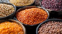 Assortment of colorful lentils and legumes in rustic bowls, showcasing red, yellow, brown, and black varieties for healthy cooking ingredients.
