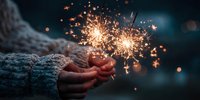 Hands holding bright sparklers creating magical golden sparks against dark evening background for celebration and festive occasions.