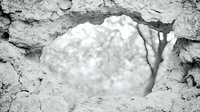 Broken concrete wall with hole revealing bright cloudy sky, creating dramatic contrast between rough textured foreground and soft background. Metaphor for freedom and escape.