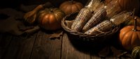 Autumn harvest display with pumpkins and corn in rustic basket on wooden table for seasonal decorating and Thanksgiving celebrations.