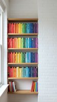 Rainbow colored books arranged by color on wooden shelves in modern white brick wall interior creating vibrant organized library display for home decor.