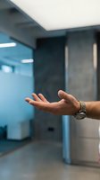 Male hand with watch extended in modern office hallway with glass partition and contemporary lighting for business communication concepts.