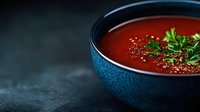 Fresh homemade tomato soup garnished with parsley and black pepper in blue ceramic bowl on dark background, appetizing comfort food styling.
