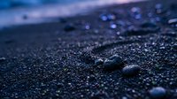 Water droplets on dark wet asphalt surface with shallow depth of field creating bokeh effect in purple and blue twilight lighting for backgrounds.