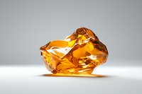 Amber-colored crystal or glass object with irregular facets and translucent surfaces catching light against neutral gray background.