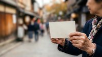 Senior man with weathered hands holding blank white card on blurred street background. Mature male displaying empty message space for text or advertising content outdoors.