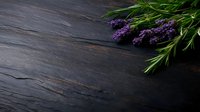 Fresh lavender sprigs with purple blooms lying on dark rustic wooden surface, moody lighting creates dramatic atmosphere for spa and wellness designs.