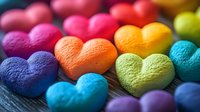 Colorful heart shaped candies arranged in rainbow pattern on dark wooden surface, macro photography showing textured details of sweet treats.