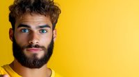 Young bearded man with curly hair and blue eyes smiling against bright yellow background for advertising and marketing campaigns.