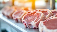 Fresh raw pork chops with bone and fat marbling arranged in row on metal tray, selective focus on meat texture with natural lighting in butcher shop.